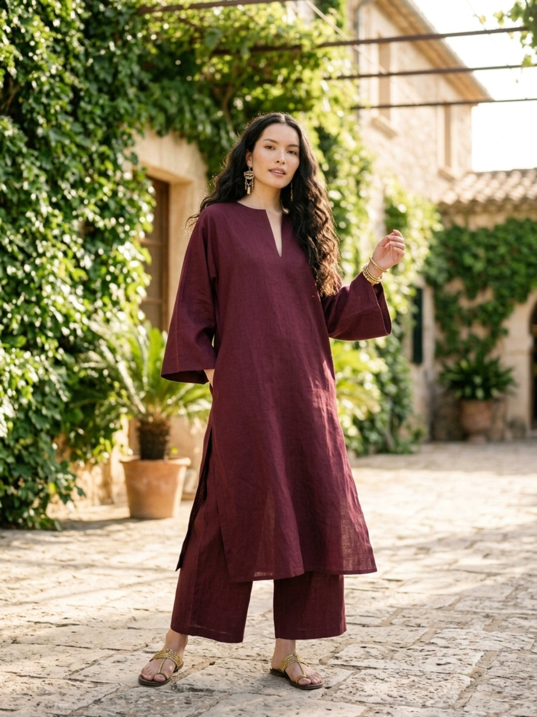 Model wearing wine cotton kurta with wide sleeves and matching wide-leg pants in an outdoor courtyard setting